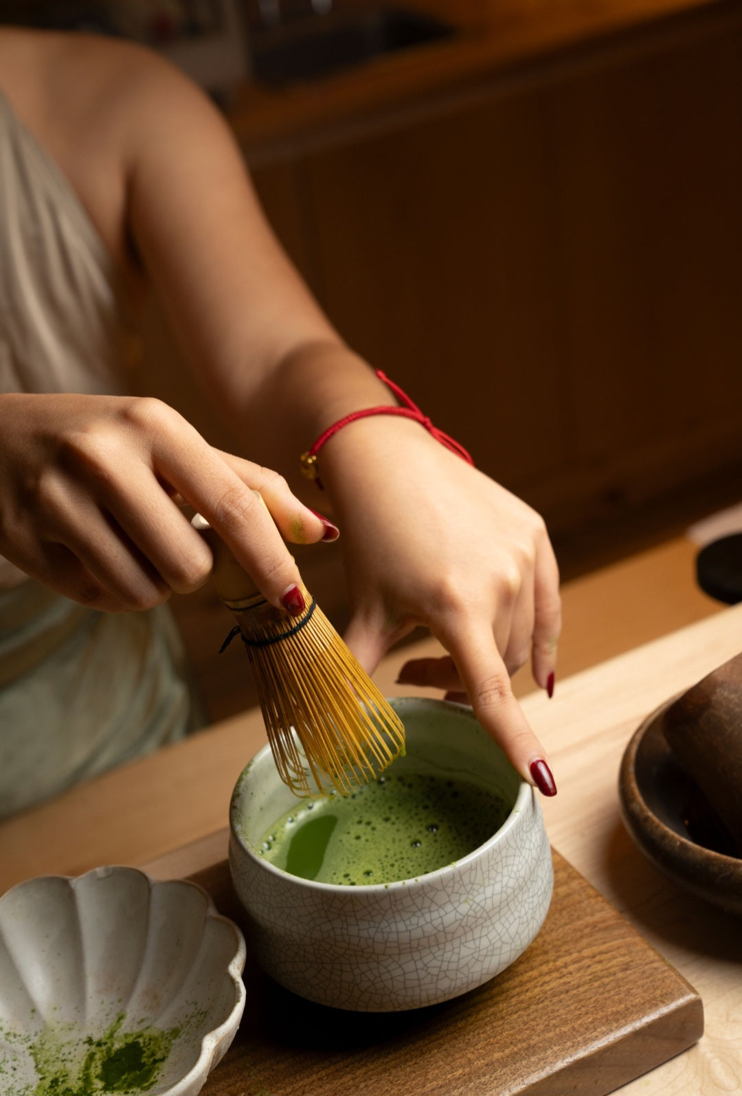 Person preparing matcha tea with a whisk on a wooden table.